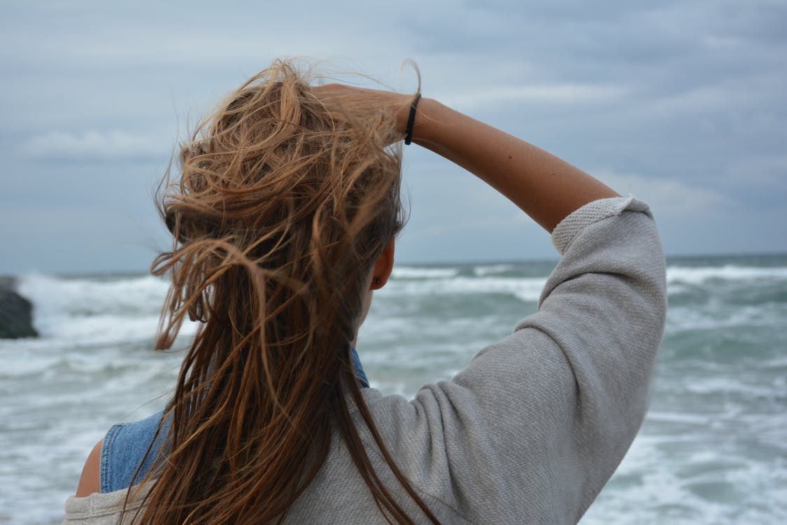mujer mirando el mar mientras se sujeta el pelo en verano