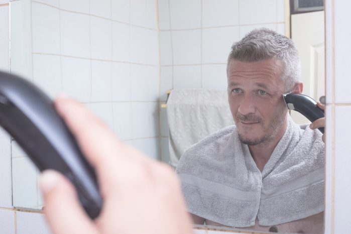 hombre cortándose el pelo frente al espejo con maquinilla